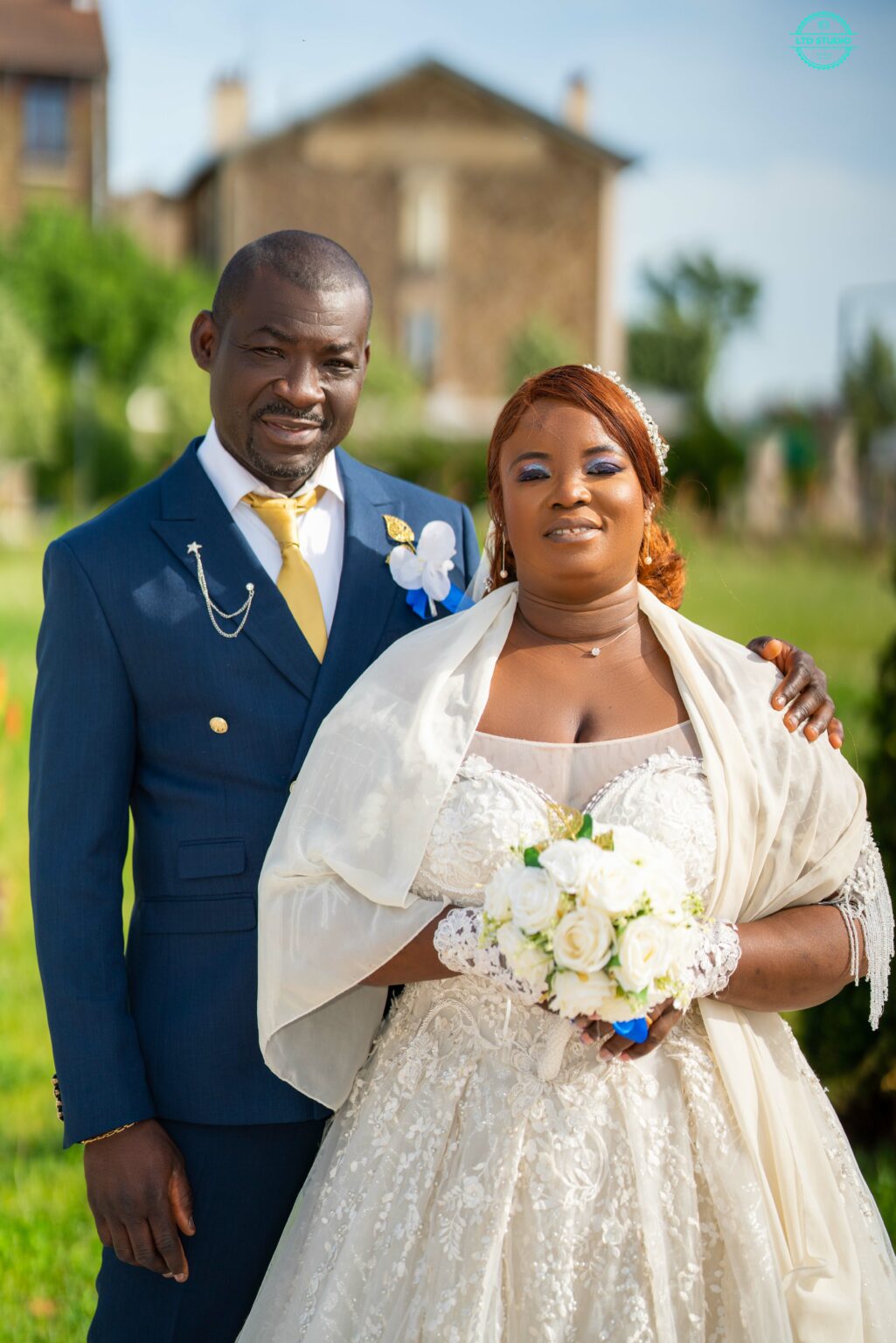 Marié en costume bleu et mariée avec son bouquet devant un château