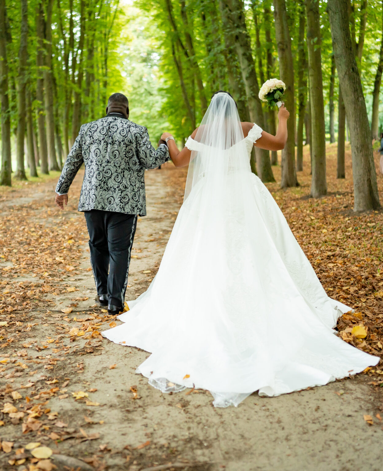 Les mariés marchant main dans la main dans une allée d'arbres en automne