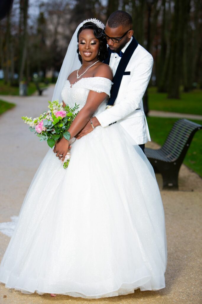 Couple de mariés enlacés dans un parc, bouquet de fleurs blanches